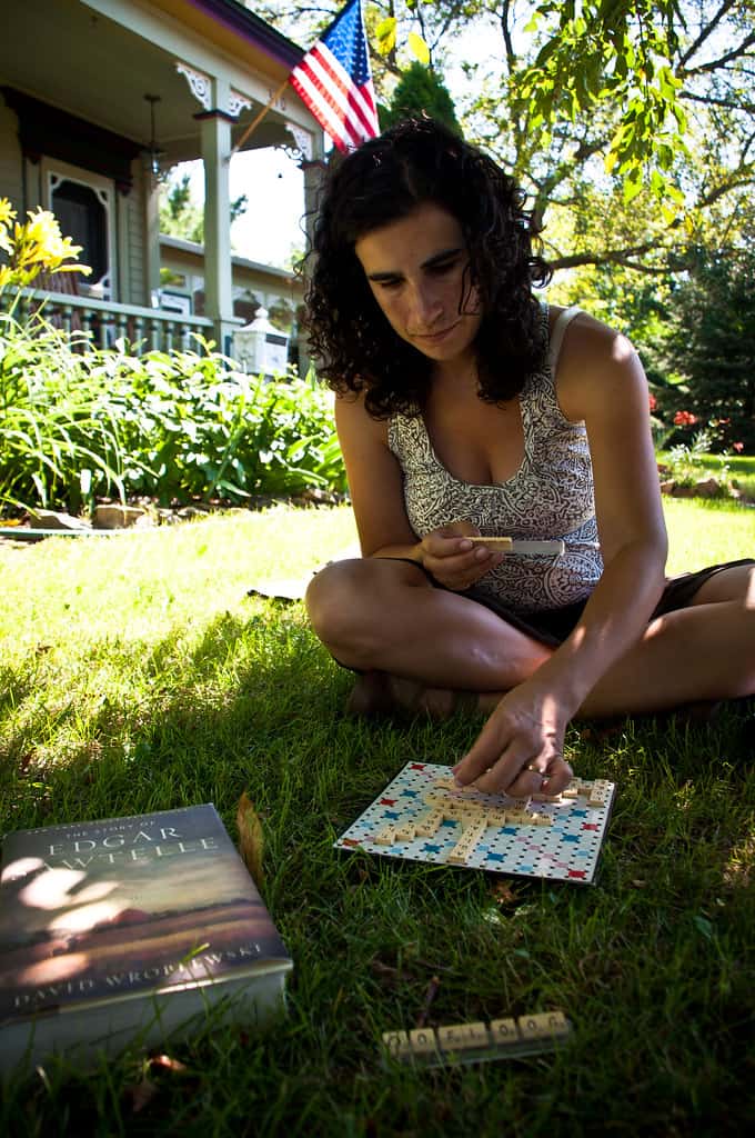 A woman is enjoying sitting on a lawn and playing a board game. Lawns should be used and not merely maintained.